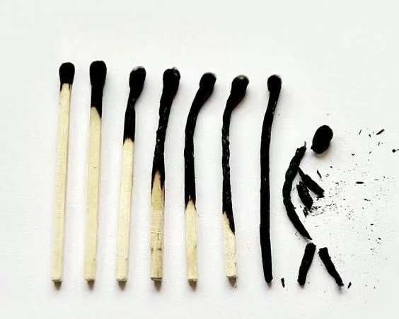 A sequence of matches gradually burning from left to right, ending with a final match arranged as a crumbling human figure made of ash, symbolizing burnout, exhaustion, and loss of energy.