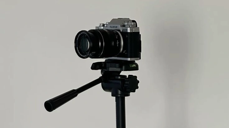 A compact mirrorless camera mounted on a tripod against a minimal neutral background, representing photography, content creation, and a clean studio setup.