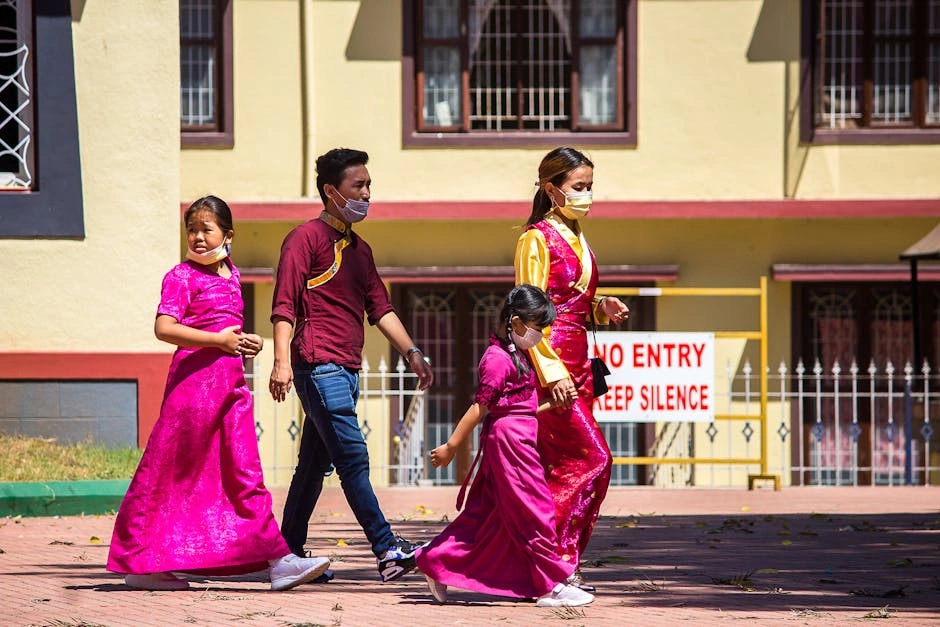 Family in vibrant traditional attire walking outside a building with a caution sign.