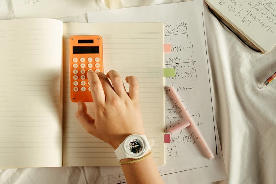 A student calculates math equations using an orange calculator and notebook for study.