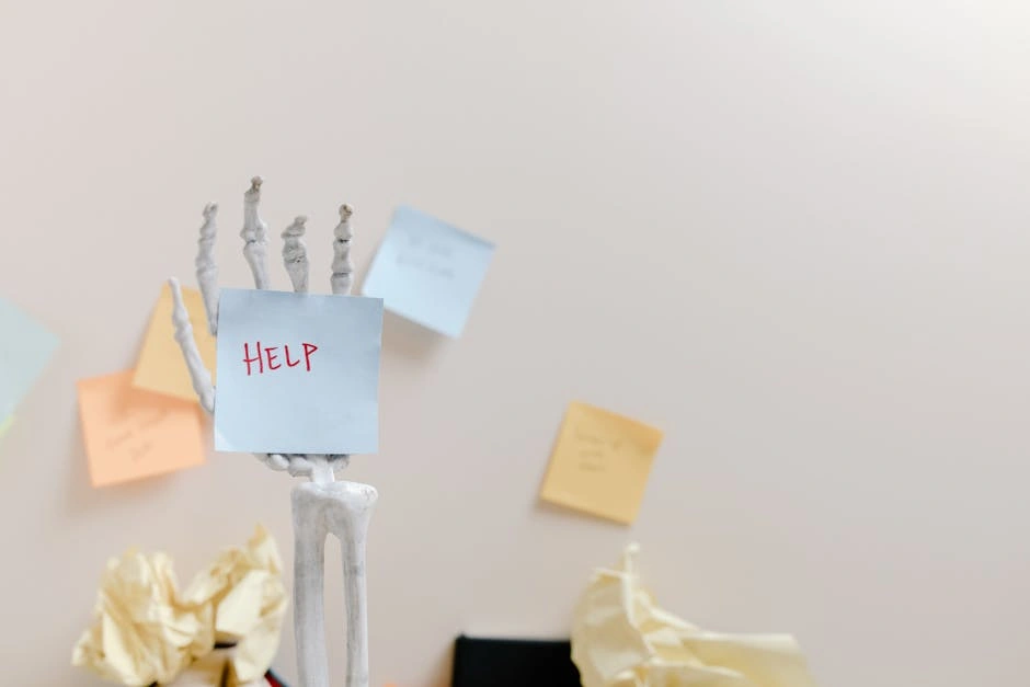 Skeleton hand holding a sticky note with 'HELP' written, against colorful notes background.