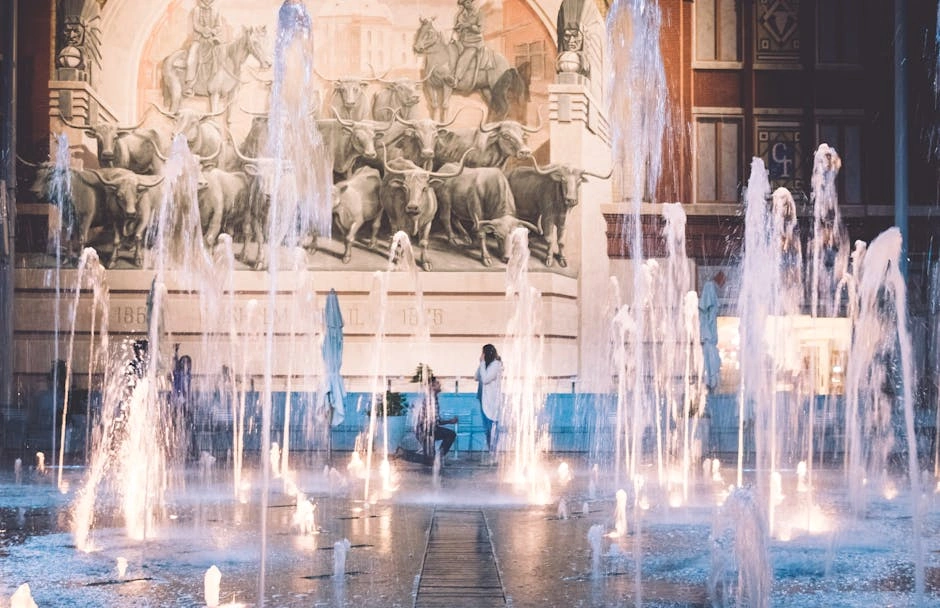 A romantic couple stands near a lively fountain in Fort Worth's iconic square, surrounded by historic artwork.