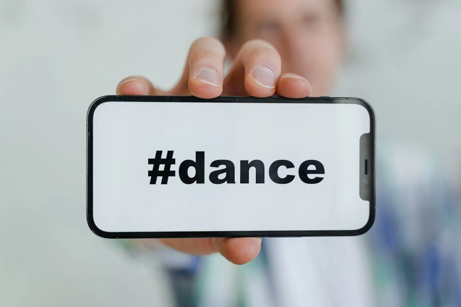 Close-up of a smartphone displaying #dance, held by a young adult.