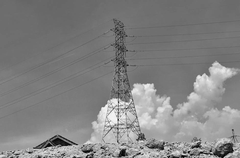 Black and white photo of a power line tower with clouds and rubble in the foreground, creating a moody atmosphere.