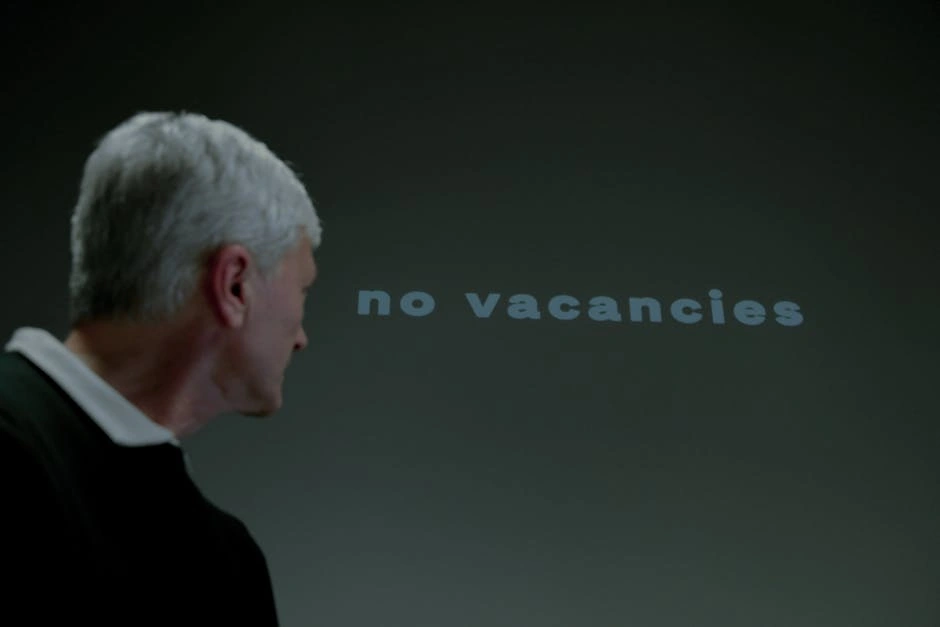 Portrait of a senior man observing a 'no vacancies' message, indicating job search rejection.
