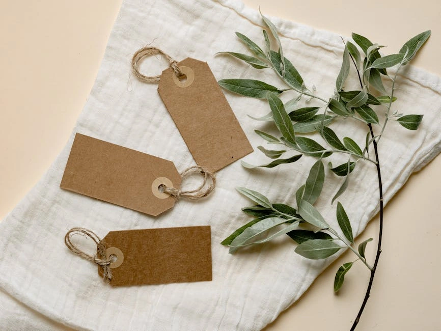 Three brown paper tags with twine on white fabric alongside green leaves. Eco-friendly design.