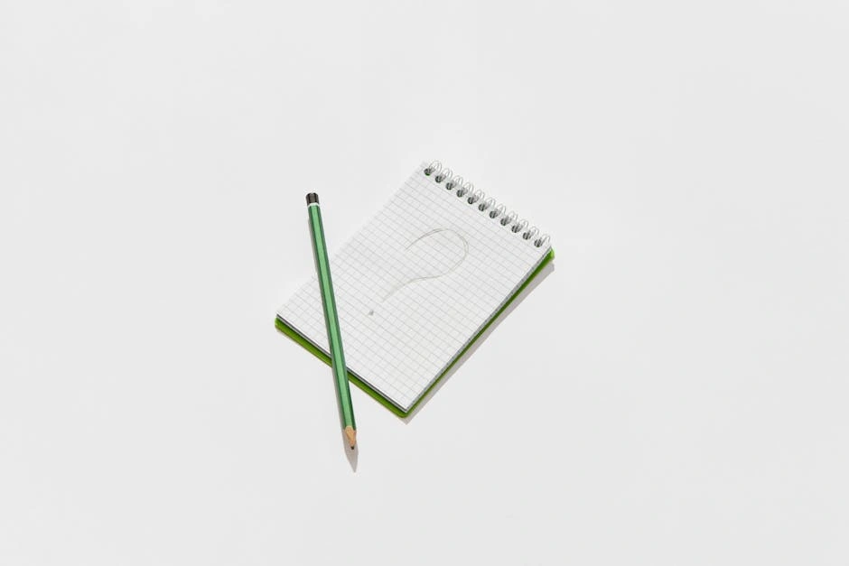 Minimalist photo of a green notepad and pencil on a white background with a drawn question mark.